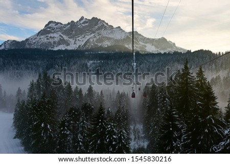 The red cable car to Pilatus mountain, pine forest covered with snow and mist, Pilatus mountain as background, winter in Switzerland.