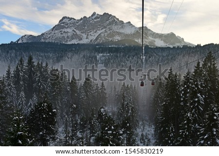 The red cable car to Pilatus mountain, pine forest covered with snow and mist, Pilatus mountain as background, winter in Switzerland.