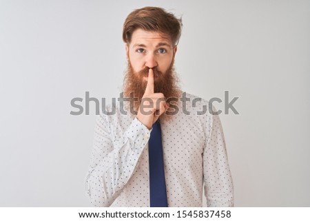 Young redhead irish businessman standing over isolated white background asking to be quiet with finger on lips. Silence and secret concept.