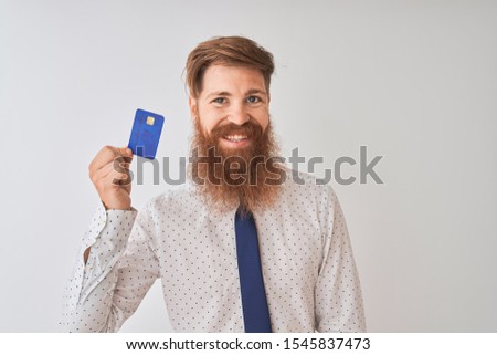 Young redhead irish businessman holding credit card standing over isolated white background with a happy face standing and smiling with a confident smile showing teeth