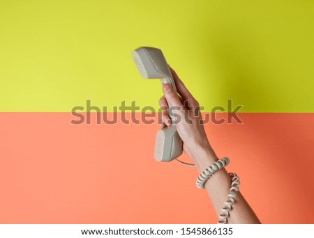 Female hand wrapped in cable holds phone tube against colored background. Port art. Creative minimalism. Top view