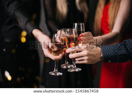 Close-up of man and woman hands clinking with champagne glasses. Four beautiful and cheerful friends in festive clothes on background.