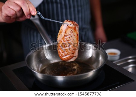 A chef fries a piece of duck. Cooking in the kitchen in a restaurant. Photo without a face. Healthy eating concept. Macro photo.
