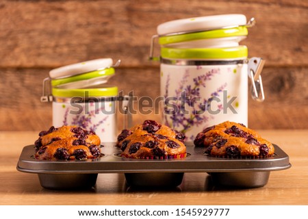 Six freshly baked banana-cherry muffins on a muffin tray and two container jars