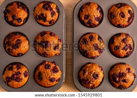 Top view of two trays banana-cherry muffins with its light brown background