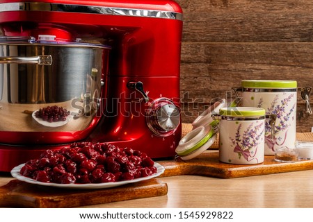 Red stand mixer, sour cherries and container jars for flour and sugar with a brown cloth