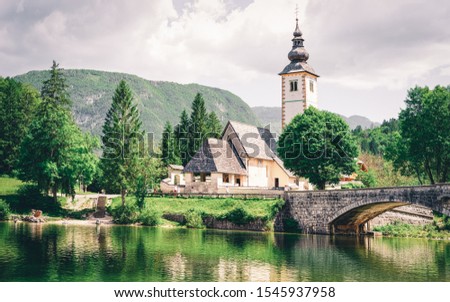 Scenery with Church of St John Baptist on Bohinj Lake at Slovenia. Nature in Slovenija. View of blue sky with clouds. Beautiful landscape in summer. Alpine Travel destination. Julian Alps mountains