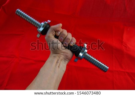 Man holding in hand Dumbbell neck with shiny thread and rubberized black handle without metal discs on a red background. Home gym equipment.