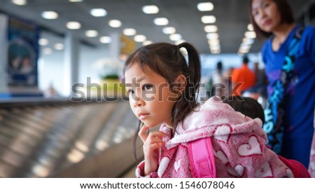 The little girl is waiting for luggage at the airport with her parent.