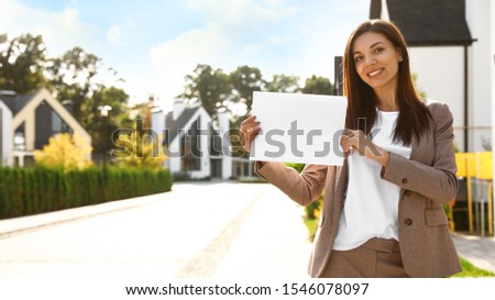 Beautiful agent holding real estate sign outdoors