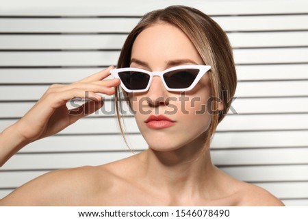 Young woman wearing stylish sunglasses against blinds