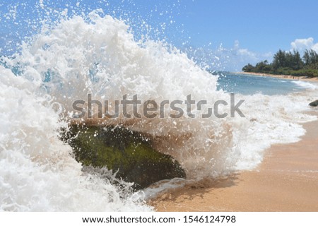 A wave crashes over a rock onto the shore.
