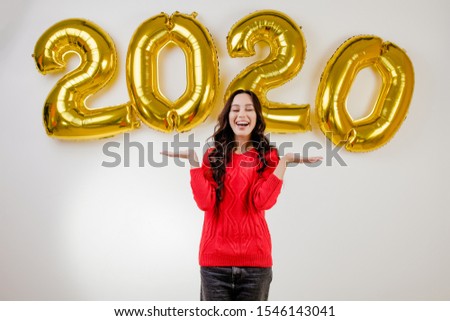 beautiful brunette woman wearing red sweater in front of 2020 new year balloons