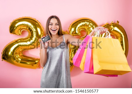 happy woman with colorful shopping bags and credit card with 2020 christmas balloons isolated over pink