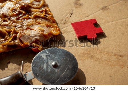 Slice of tasty traditional Italian pizza with pastry wheel and bright red puzzle piece on a marble counter in a conceptual image