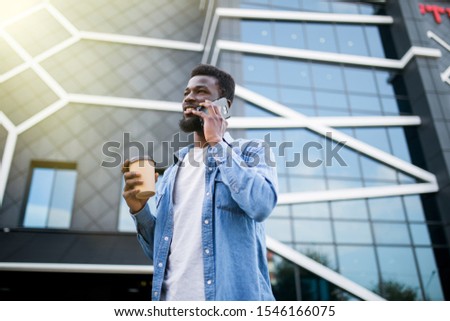 Handsome african man talking on phone at park. Young black man talking on cellphone while sitting on bench outdoor. African american smiling guy in a happy conversation at mobile phone.