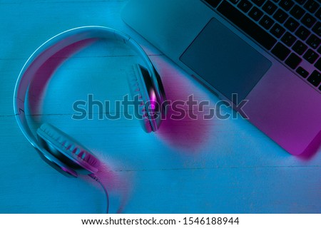 Top view of set of gadgets in purple neon light and blue background. Laptop and headphones on wooden table. Copyspace for your advertising. Tech, modern, gadgets.