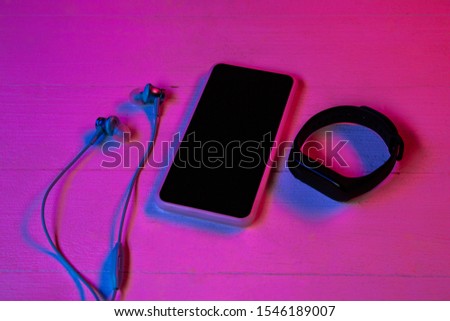 Top view of set of gadgets in purple neon light and pink background. Smartphone and smartwatch, headphones. Copyspace for your advertising. Tech, modern, gadgets.