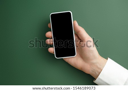 Male hand holding smartphone with empty screen on green background for text or design. Blank gadget templates for contact or use in business. Finance, office, purchases. Mock up. Copyspace.