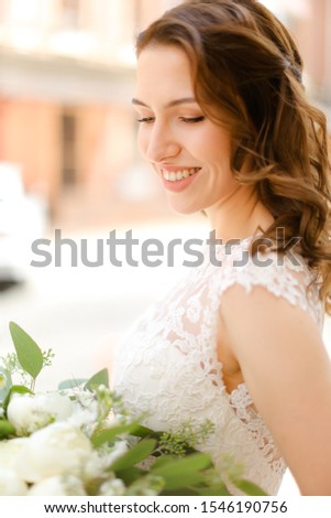 Happy beautiful fiancee keeping bouquet of flowers and wearing white dress. Concept of bridal photo session and wedding.