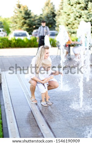 Young happy mother sitting with little baby outside near fountain. Concept of walking in city and motherhood.