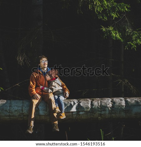 Father and son sitting together outdoors spending good time on dark nature background copy space. Happy family dad kid hugging with love at forest walk natural light. Happiness Christmas holidays