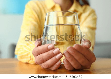 Woman holding glass of water at wooden table, closeup. Refreshing drink