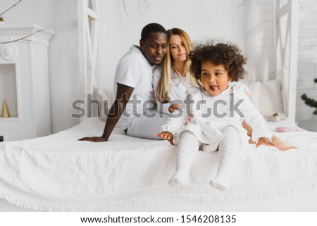 Excited multiracial young family with little girl child have fun, overjoyed happy. international mom and dad play with small girl, enjoy weekend at home together