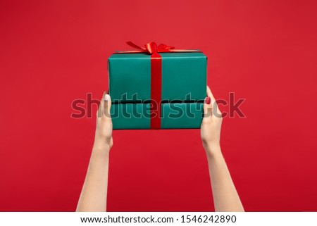 cropped view of woman holding green wrapped Christmas presents with ribbon isolated on red background. Christmas concept