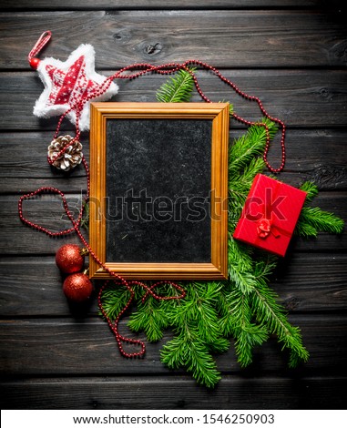 Photo frame with Christmas decorations and fir branches. On a dark wooden background