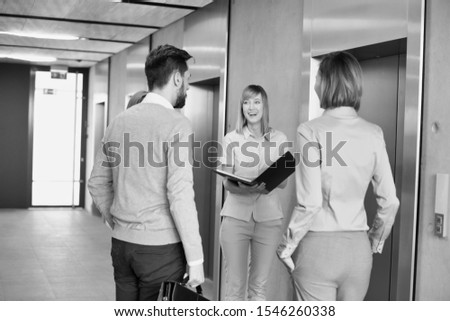 Black and white photo of business people discussing over document while waiting for elevator