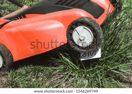 close up view of electric lawn mower cutting a bush with a sign please stop