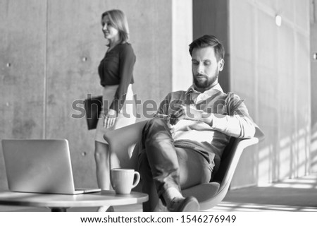 Black and white photo of businessman using smartphone while sitting in office lobby