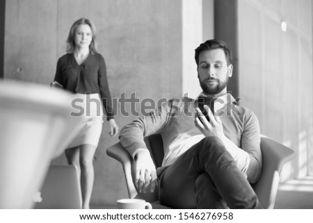 Black and white photo of businessman using smartphone while sitting in office lobby