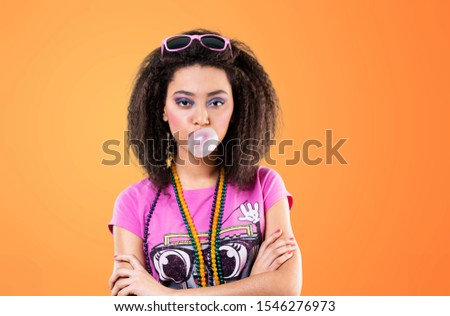 Dark-eyed girl with pink makeup chewing bubble gum. Studio photo of relaxed african lady isolated on yellow background.