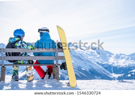 Photo from back of athletes sitting on bench next to snowboard in ski resort