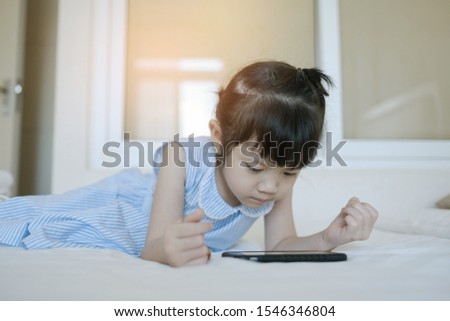 asian Chinese girl playing smartphone on bed, watching smartphone, kid use phone and play game, child use mobile, addicted game and cartoon
