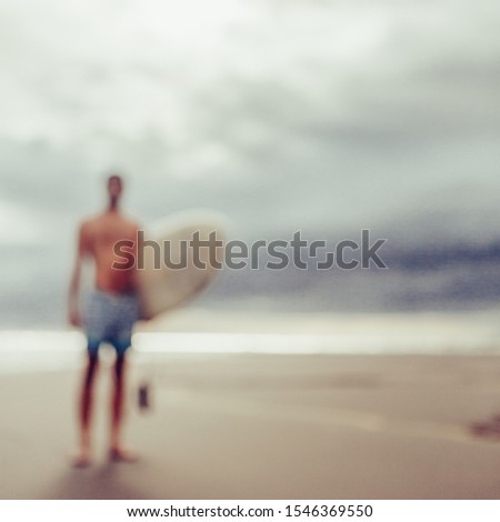Out of focus, blurry image of handsome man with surfboard stand at sand of surf spot at sea ocean beach after surfing. Concept of sport, freedom, happiness, new modern life, hipster, generation Y.