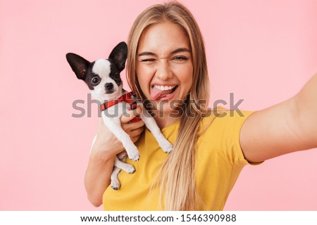 Cute lovely cheerful girl taking a selfie while playing with her pet chihuahua isolated over pink background
