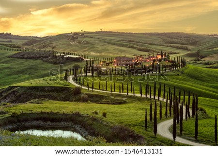 Tuscany, Crete Senesi rural sunset landscape. Countryside farm, cypresses trees, green field, sun light and cloud. Italy, Europe. Royalty-Free Stock Photo #1546413131