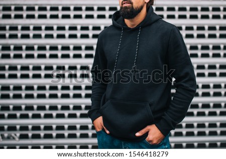 City portrait of handsome hipster guy with beard wearing black blank hoodie or hoody with space for your logo or design. Mockup for print