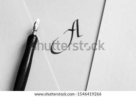 Sheets of white paper with handwritten letter A, next to a pen and a bottle of ink. The concept of learning calligraphy, letters. Minimalism, place for text.