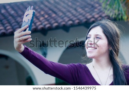 Colorful photo of a beautiful young girl dressed in a blouse shirt and white pants, taking a picture of herself with her smart phone. Concept of feminine beauty. Horizontal image