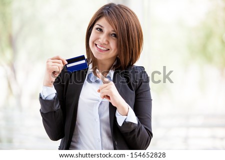Gorgeous female Asian bank representative holding a credit card in one hand and pointing at it with the other
