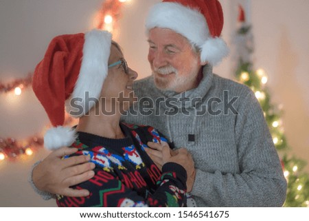 A senior couple smiling looking each other in the eyes. Wearing Santa Claus hats celebrating Christmas holidays.  Love and serenity concept