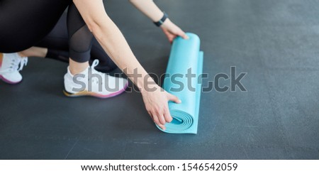 Young woman rolls up a yoga mat after fitness workout
