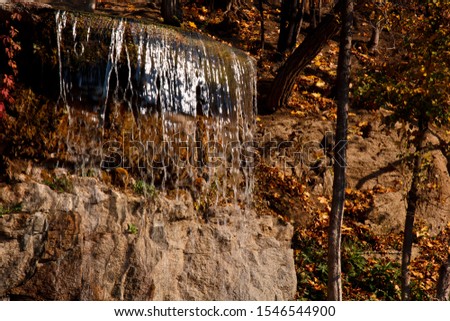 Waterfall from stones in the park. Against the background of autumn foliage and trees of orange and yellow