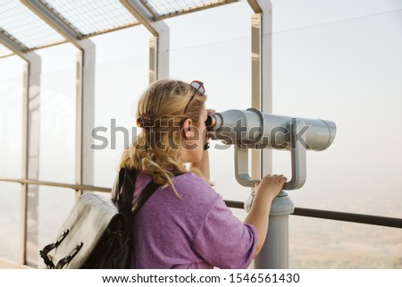 The woman looks with binoculars from the top of the tower 