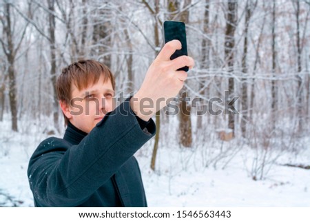 A man in a coat takes a selfie in a snowy forest