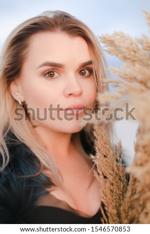 Portrait of nice girl wearing fur coat with dried plants bouquet in snowed field background. Concept of winter photo session and beauty, fashionable female person.